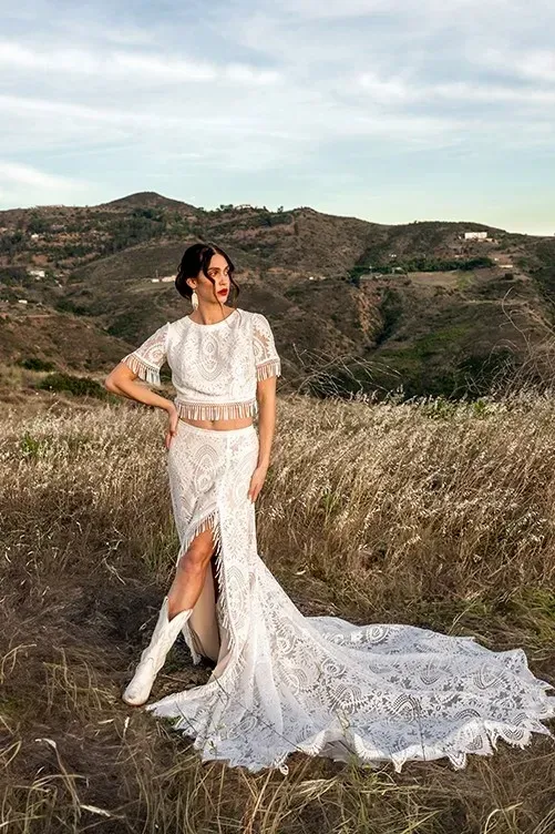 A woman in a wedding dress and cowboy boots is standing in a field.