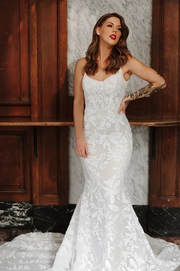 A woman in a white wedding dress is standing in front of a wooden wall.