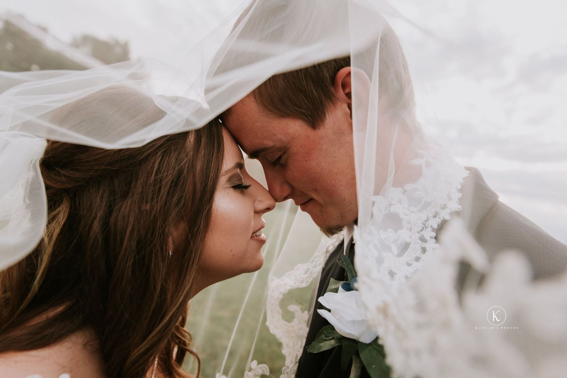 A bride and groom are kissing under a veil.
