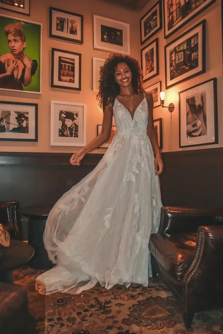 A woman in a wedding dress is standing in a room with pictures on the wall.