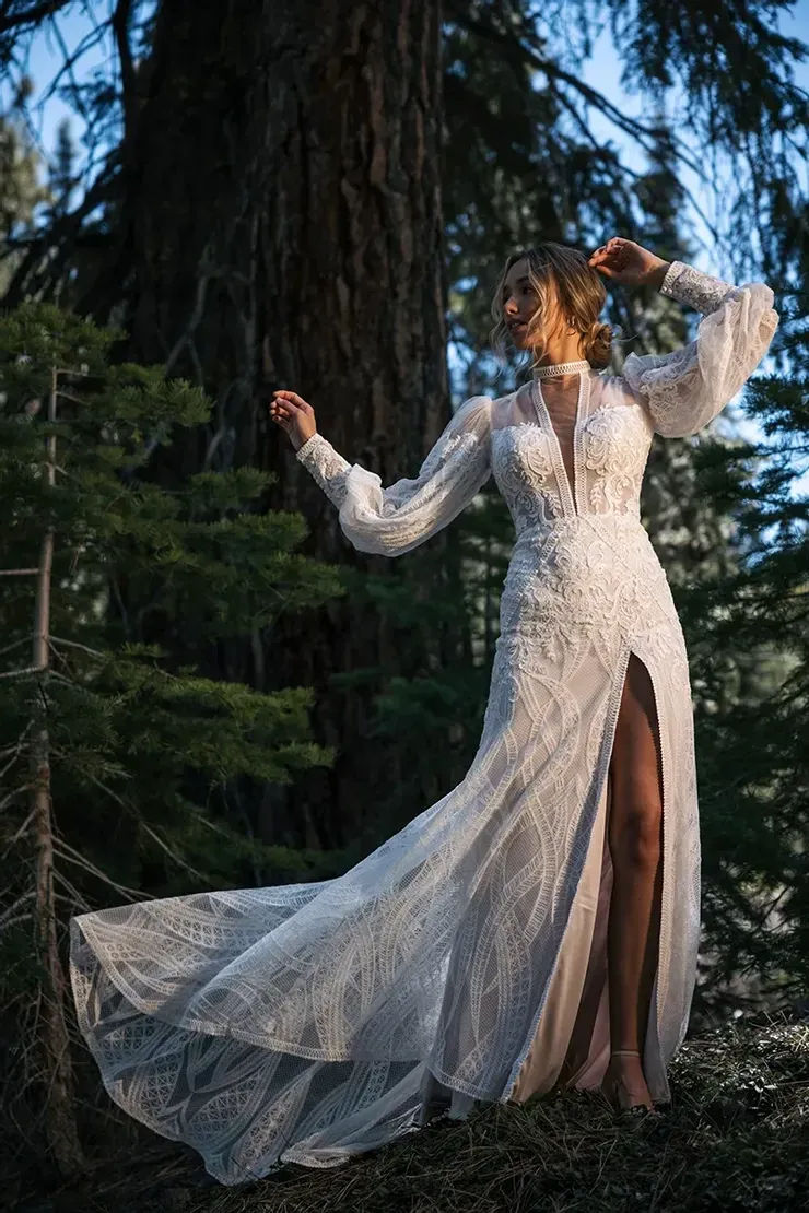 A woman in a wedding dress is standing next to a tree in the woods.