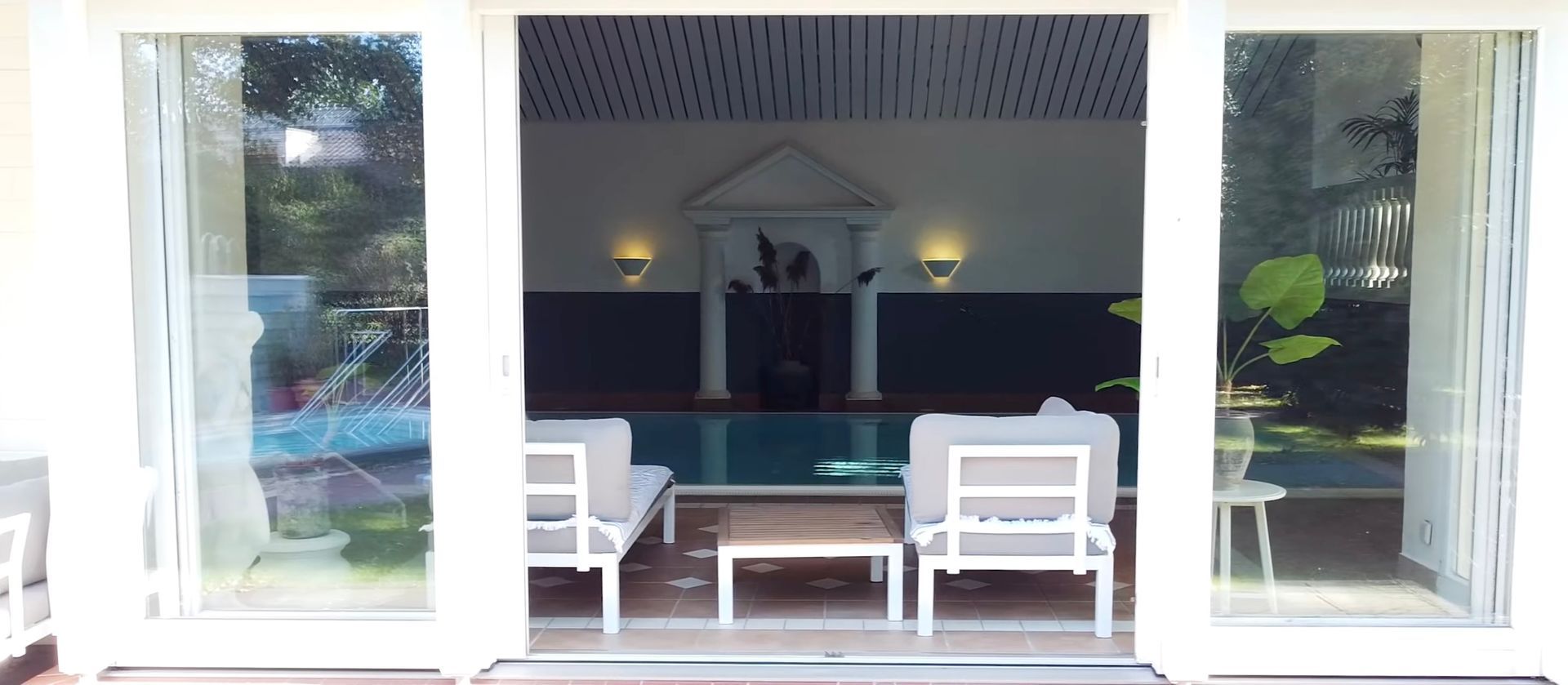 Durch die Glasschiebetüren eines Hauses ist ein Swimmingpool sichtbar.