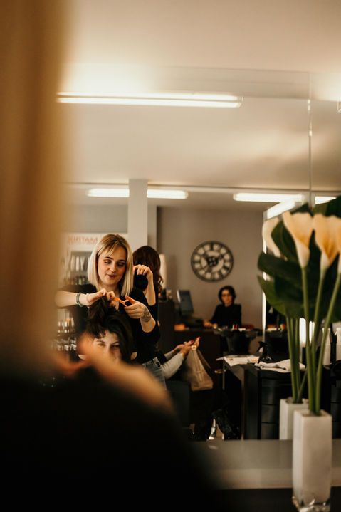 Une femme prend un selfie devant un miroir dans un salon à l'éclairage tamisé, avec des fleurs au premier plan.