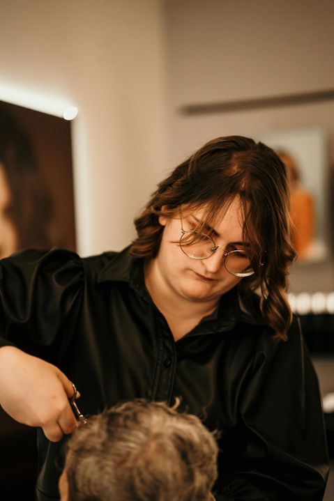 Coiffeur en chemise noire coupant les cheveux d'un client dans un salon