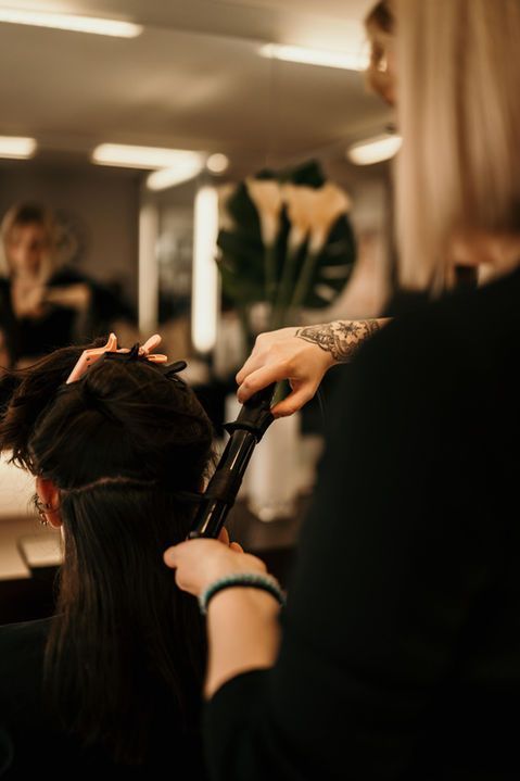 Une coiffeuse boucle les cheveux d'une cliente dans un salon, sur fond d'éclairage doux et chaleureux.