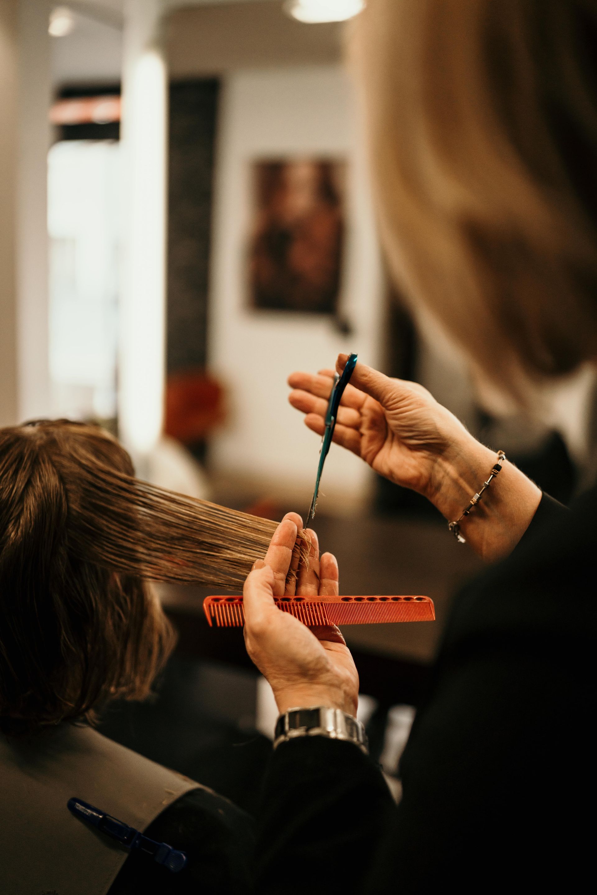 Une coiffeuse coupe les cheveux d'une cliente avec des ciseaux et un peigne dans un salon de coiffure.