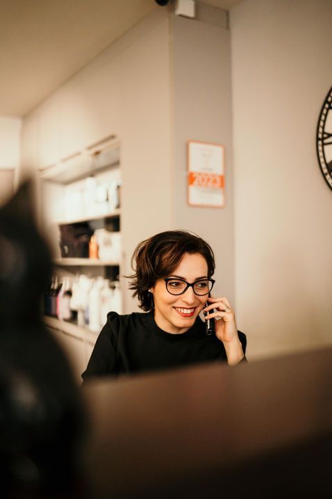 Une personne portant des lunettes sourit en parlant au téléphone dans un café à l'éclairage tamisé.