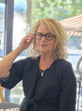 Femme assise en haut noir ajustant ses lunettes à la terrasse d'un café aux fenêtres lumineuses et à la terrasse.