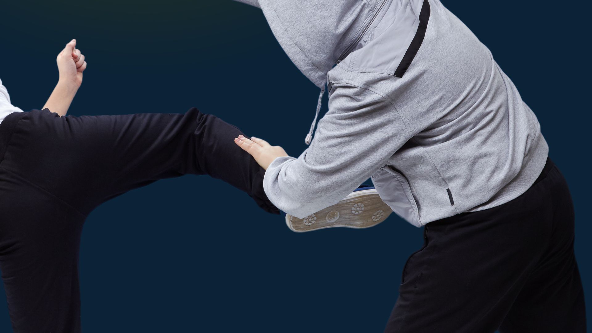 Person kicking a person wearing a grey hooded sweatshirt; self-defense.