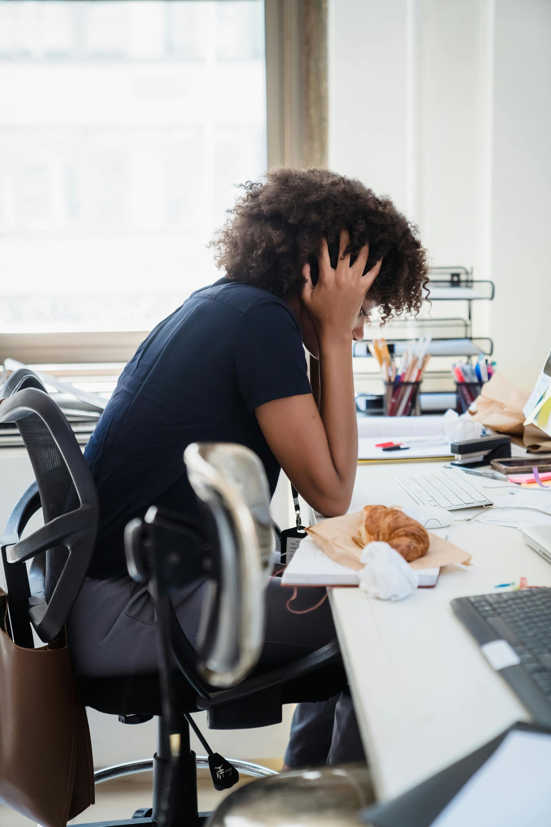 A busy woman professional is sitting at a desk with her head in her hands. She is stressed out.
