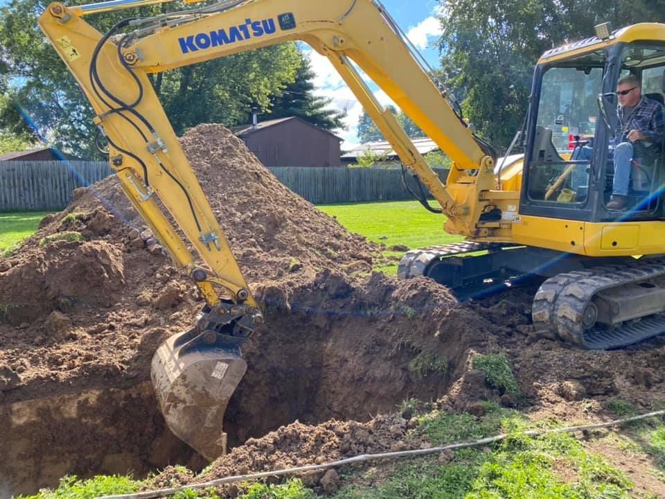Yellow Komatsu excavator digging a dirt trench beside a large soil pile outdoors