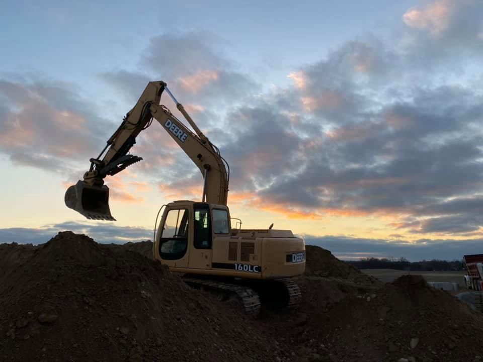 Yellow excavator on a dirt pile at dusk under a cloudy sky