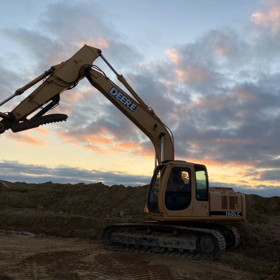 Yellow John Deere excavator silhouetted at sunset on a dirt site