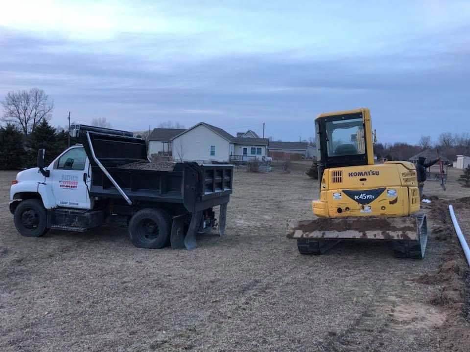 White dump truck and yellow skid steer in a muddy field near houses at dusk