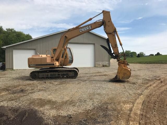 Yellow excavator beside a gray metal building on a gravel lot under a cloudy sky