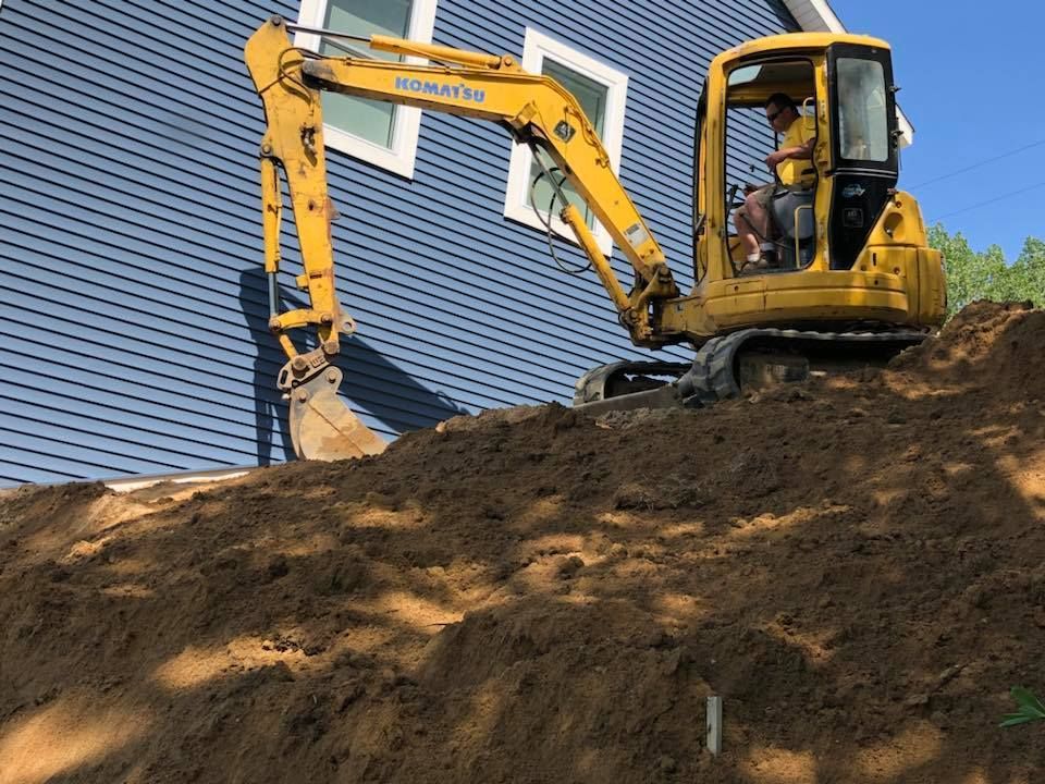 Yellow excavator digging dirt on a hillside beside a blue-roofed building