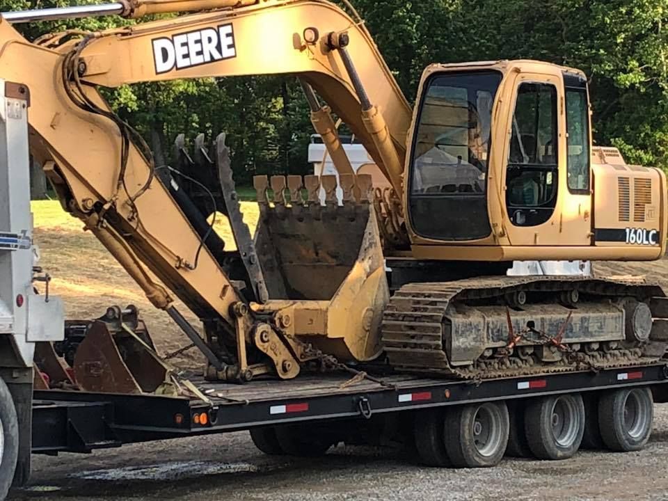 Yellow Deere excavator on a flatbed trailer outdoors, loaded for transport.