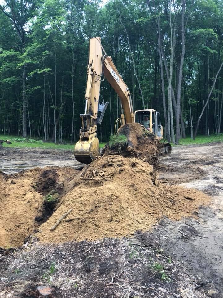 Yellow excavator digging a trench in a muddy forest clearing with dirt piled around it
