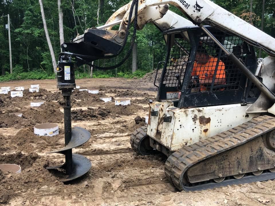 Tracked skid steer drilling into muddy ground on a construction site with a forest background