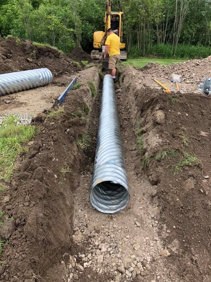 Worker installing a large corrugated drainage pipe in a dirt trench at a construction site