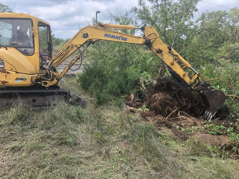 Yellow excavator clearing brush in a grassy field near trees