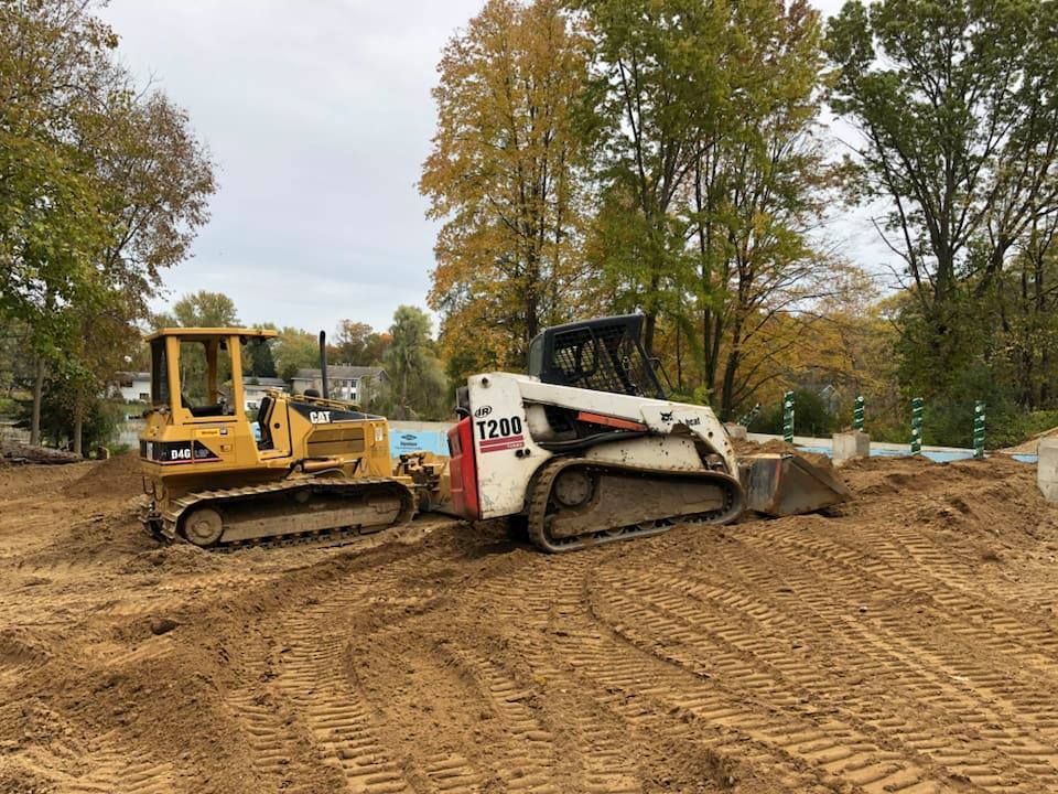 Two construction machines on a dirt site, with a white skid steer in front of a yellow bulldozer.