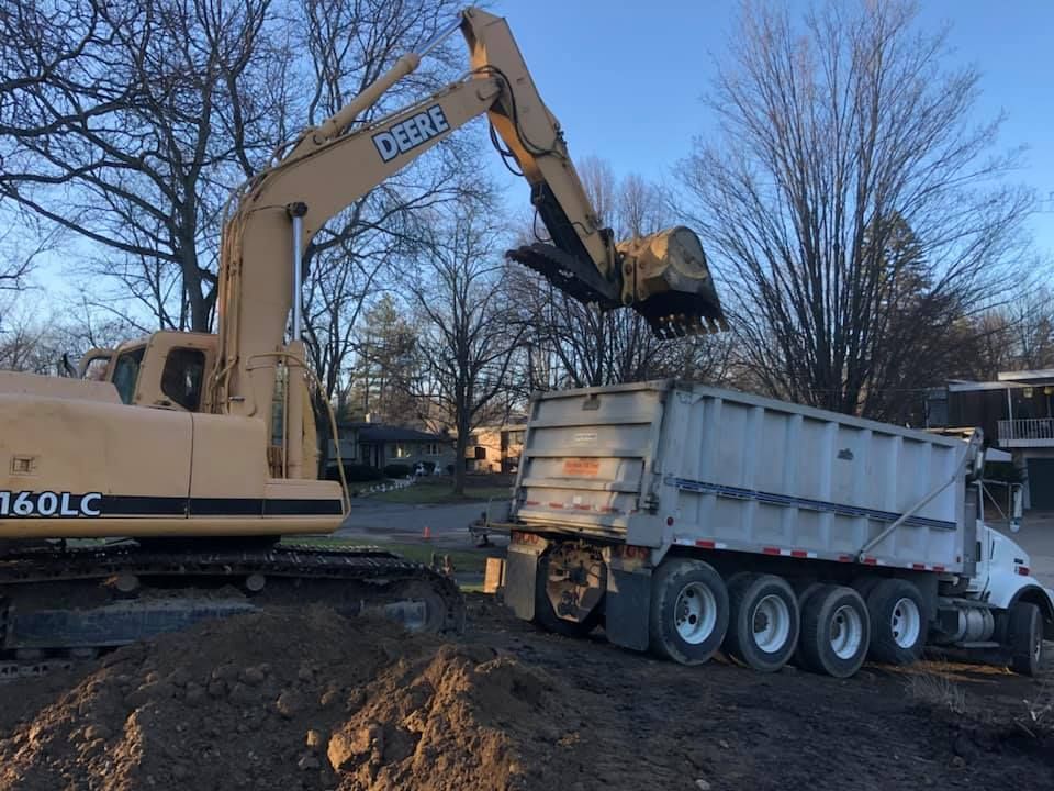 Excavator loading dirt into a dump trailer at a construction site on a sunny day