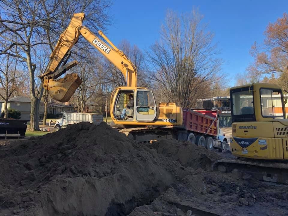 Excavator loading dirt into a red dump truck at a construction site on a sunny day