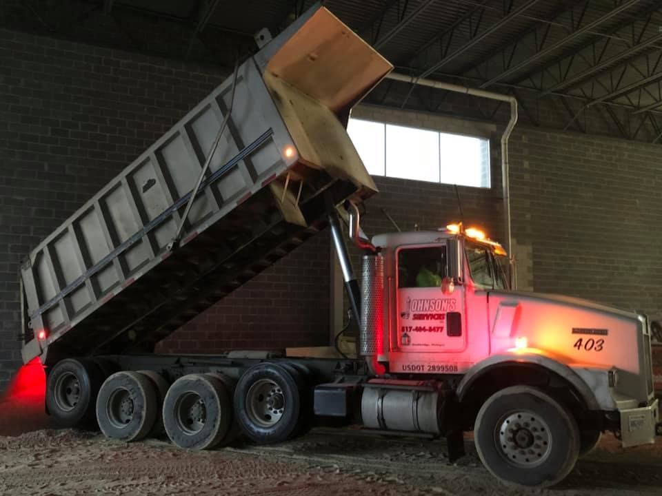 Black dump truck raising bed under warehouse lights at night