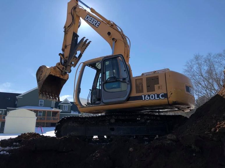 Yellow excavator on a dirt mound under a blue sky at a construction site