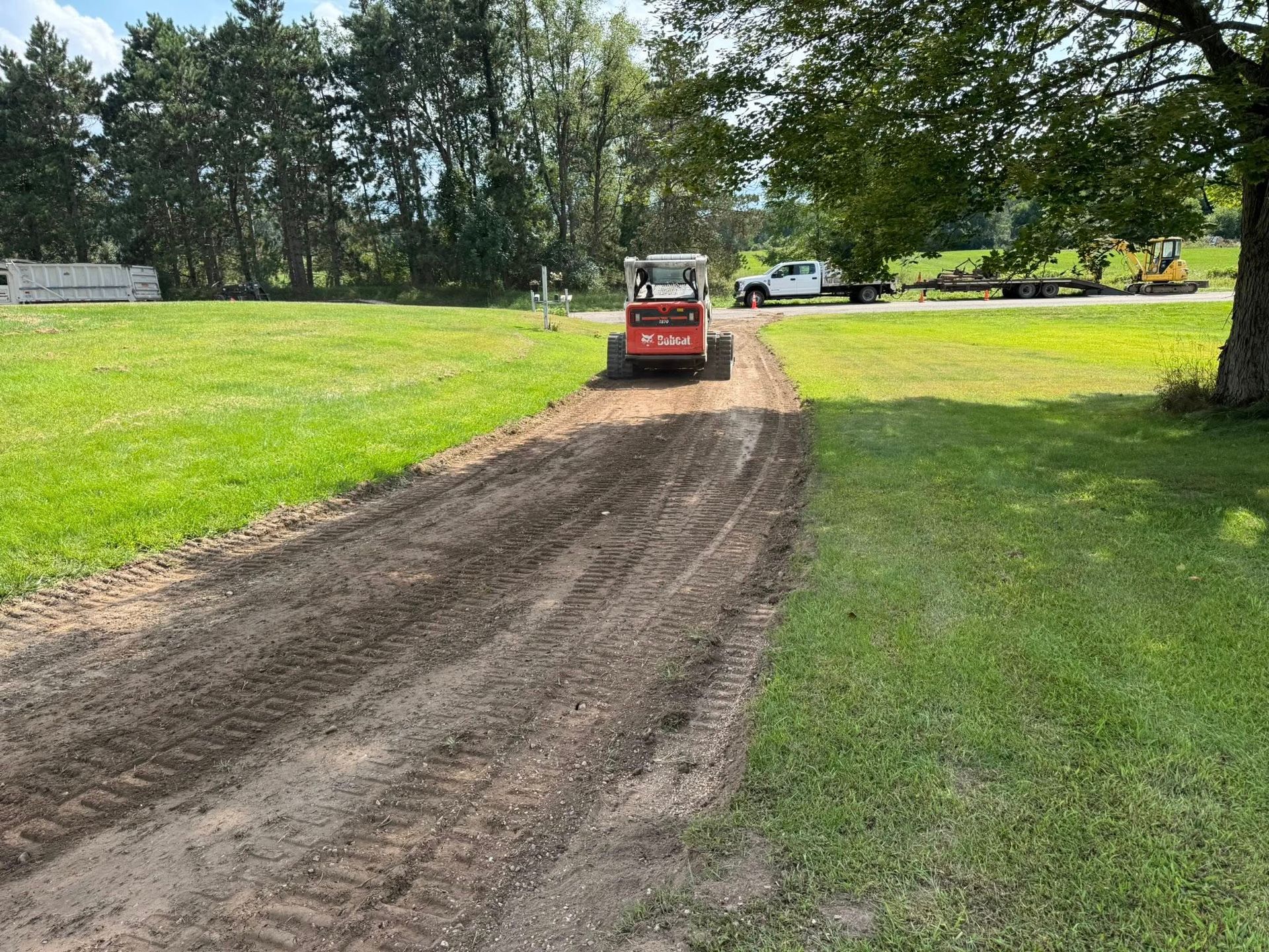 Small red skid steer smoothing a dirt path through a grassy park