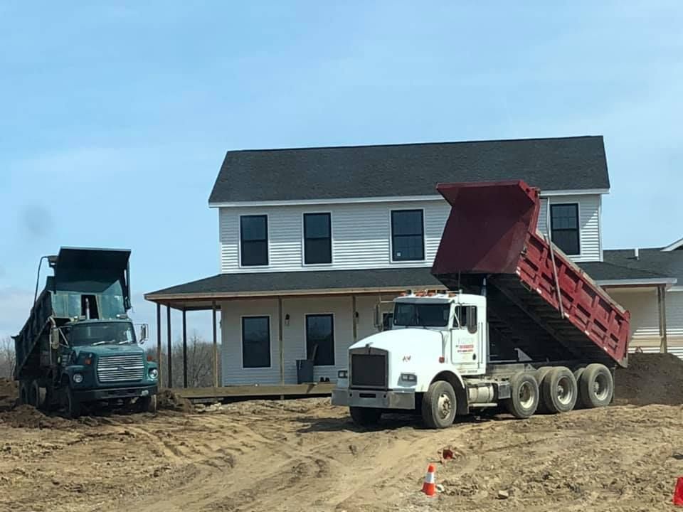 Dump trucks at a construction site beside a newly built two-story house.