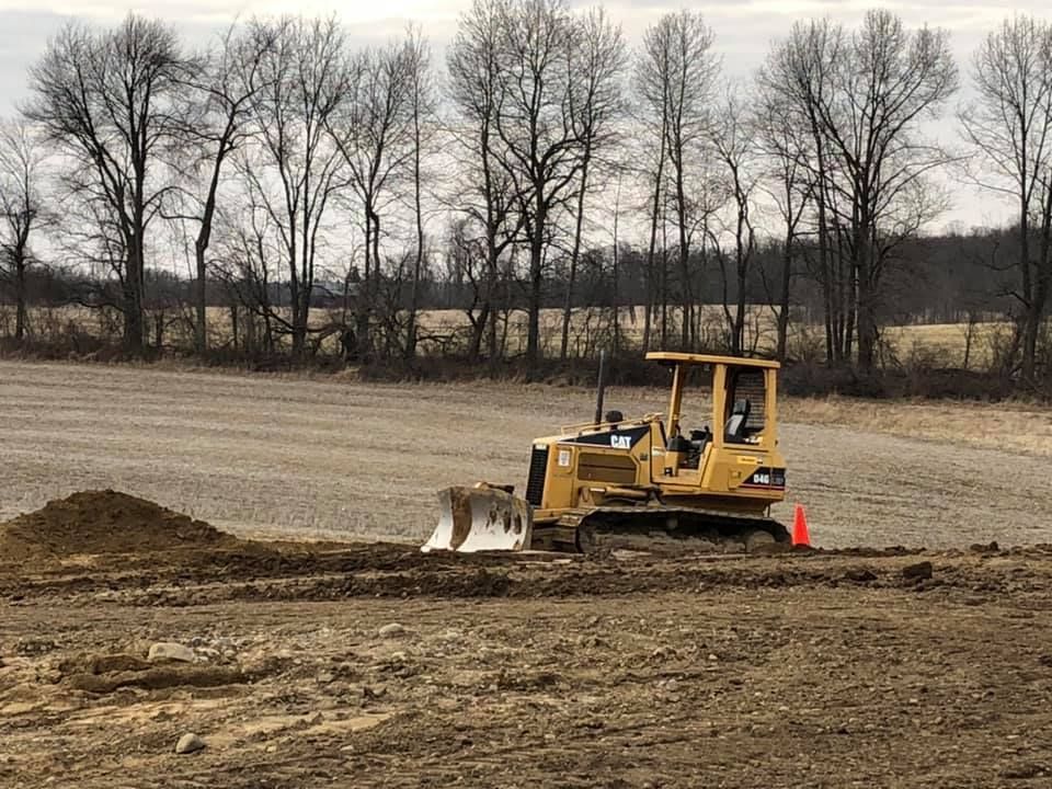 Yellow bulldozer grading dirt in a field with leafless trees in the background