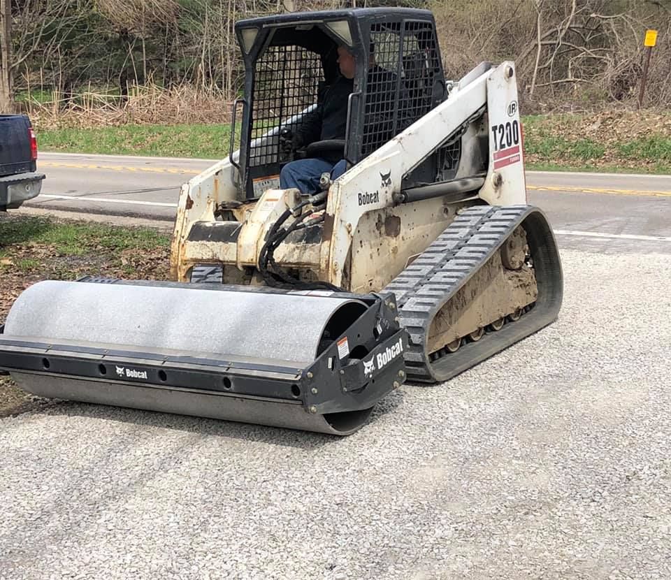 White Bobcat skid steer with brush cutter attachment parked on a roadside shoulder.