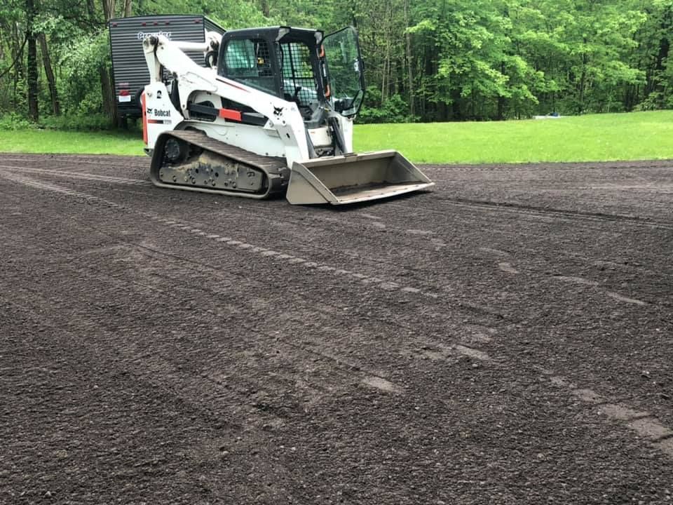 Skid steer spreading gravel on a driveway beside green trees