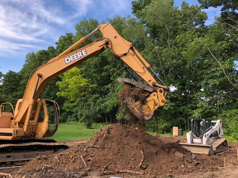 Excavator lifting a large clump of dirt at a construction site with trees in the background