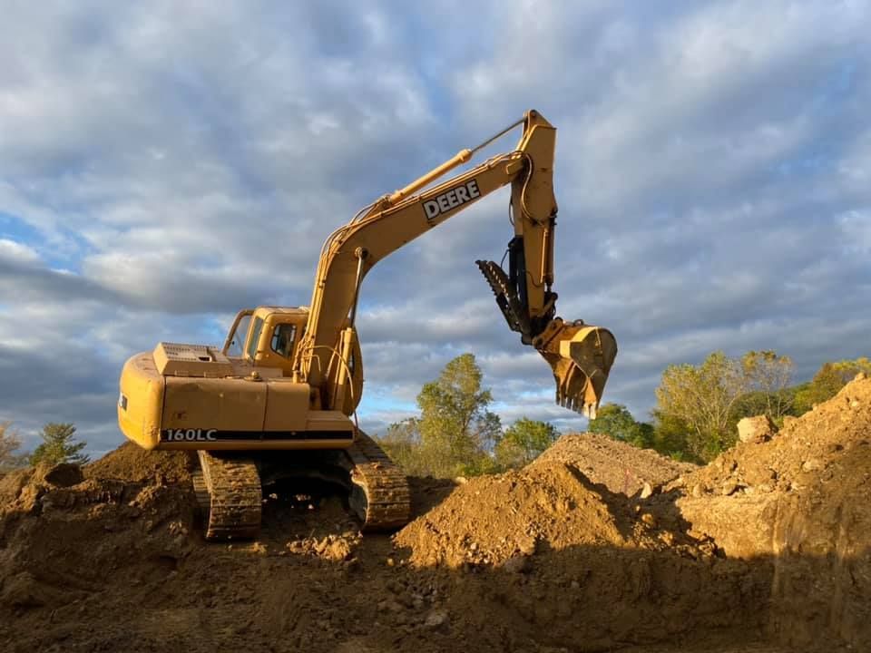 Yellow excavator digging dirt on a muddy construction site under a cloudy sky