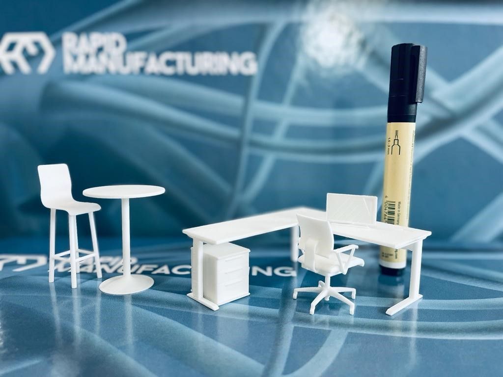 Ein Miniatur-Büroset mit einem Marker vor einem Rapid Manufacturing-Logo