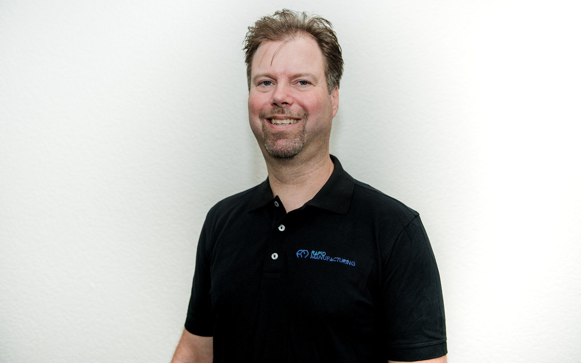Ein Mann in einem schwarzen Poloshirt lächelt in die Kamera.