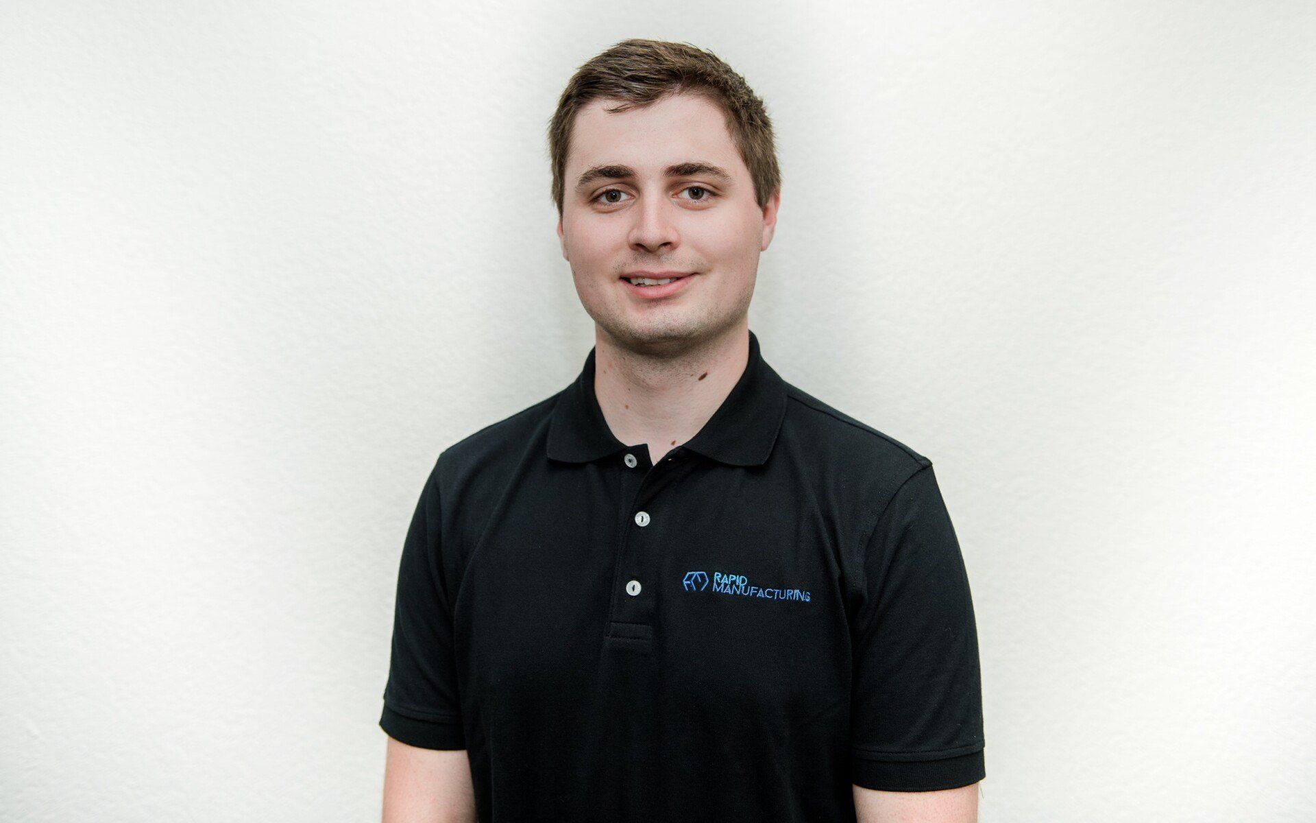 Ein Mann in einem schwarzen Poloshirt lächelt in die Kamera.