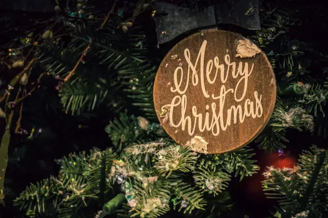 An einem Weihnachtsbaum hängt ein „Frohe Weihnachten“-Schild.