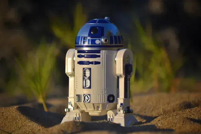 Ein Spielzeug-R2D2 aus Star Wars sitzt im Sand.