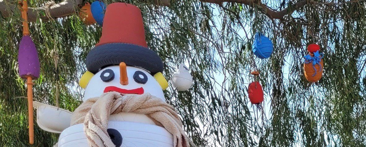 Ein ausgestopfter Schneemann mit Mütze und Schal hängt an einem Baum.