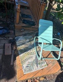 Turquoise patio chair on a wooden deck beside a patterned outdoor rug in a sunny backyard.