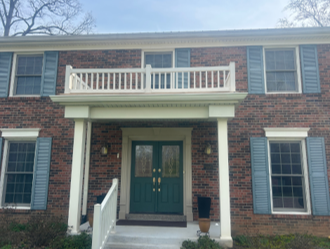 Brick house front entrance with teal door, white balcony, and shutters