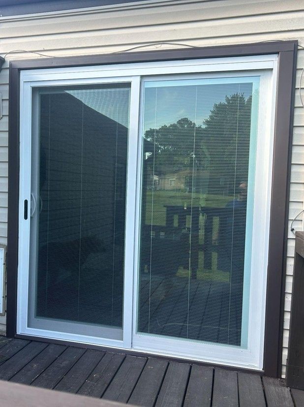 Sliding glass patio door with white frame and blinds, reflecting a backyard.