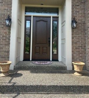 Front entrance with dark wooden door, sidelights, brick walls, and two planters on a stone walkway. Front entrance with dark wooden door, sidelights, brick walls, and two planters on a stone walkway.