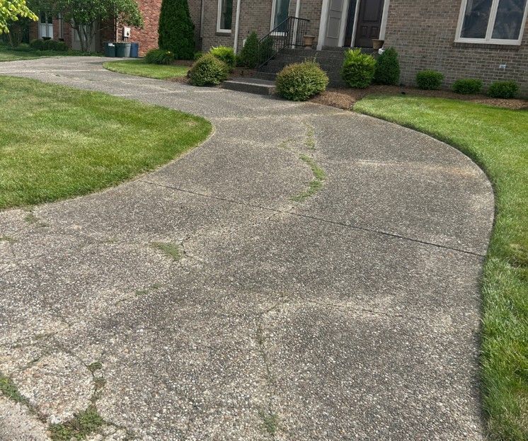 Cracked concrete walkway curving through a front yard beside a brick house.