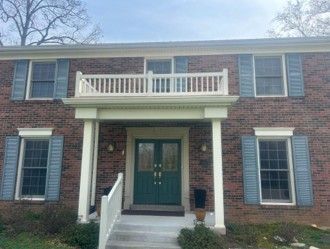 Brick two-story house with green front door, white balcony, and blue shutters on the windows. Brick two-story house with green front door, white balcony, and blue shutters on the windows.