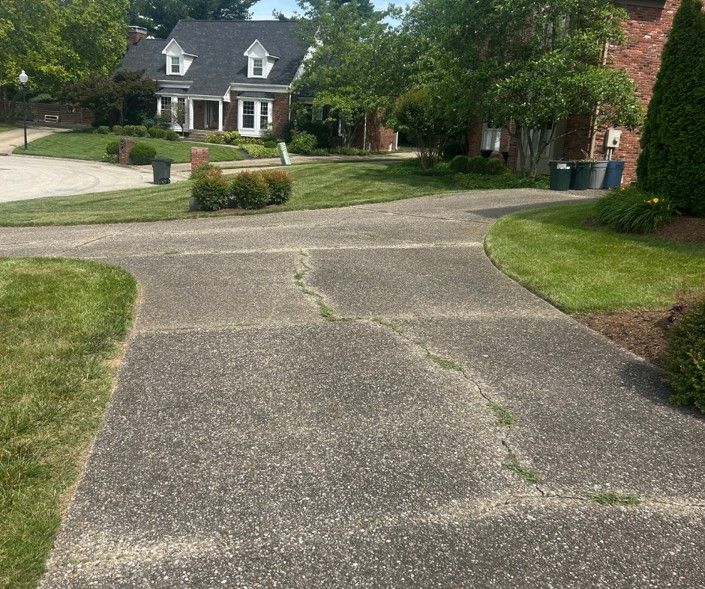 Residential driveway with a cracked concrete apron leading to a suburban house and lawn.